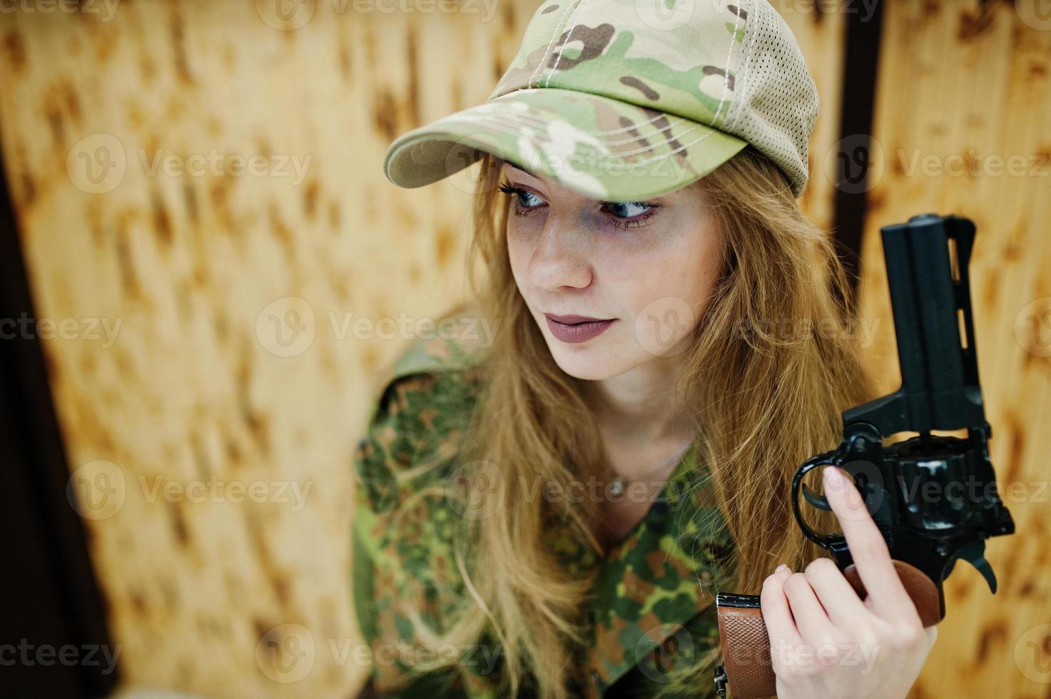 Military girl in camouflage uniform with revolver gun at hand against army background on shooting range. photo