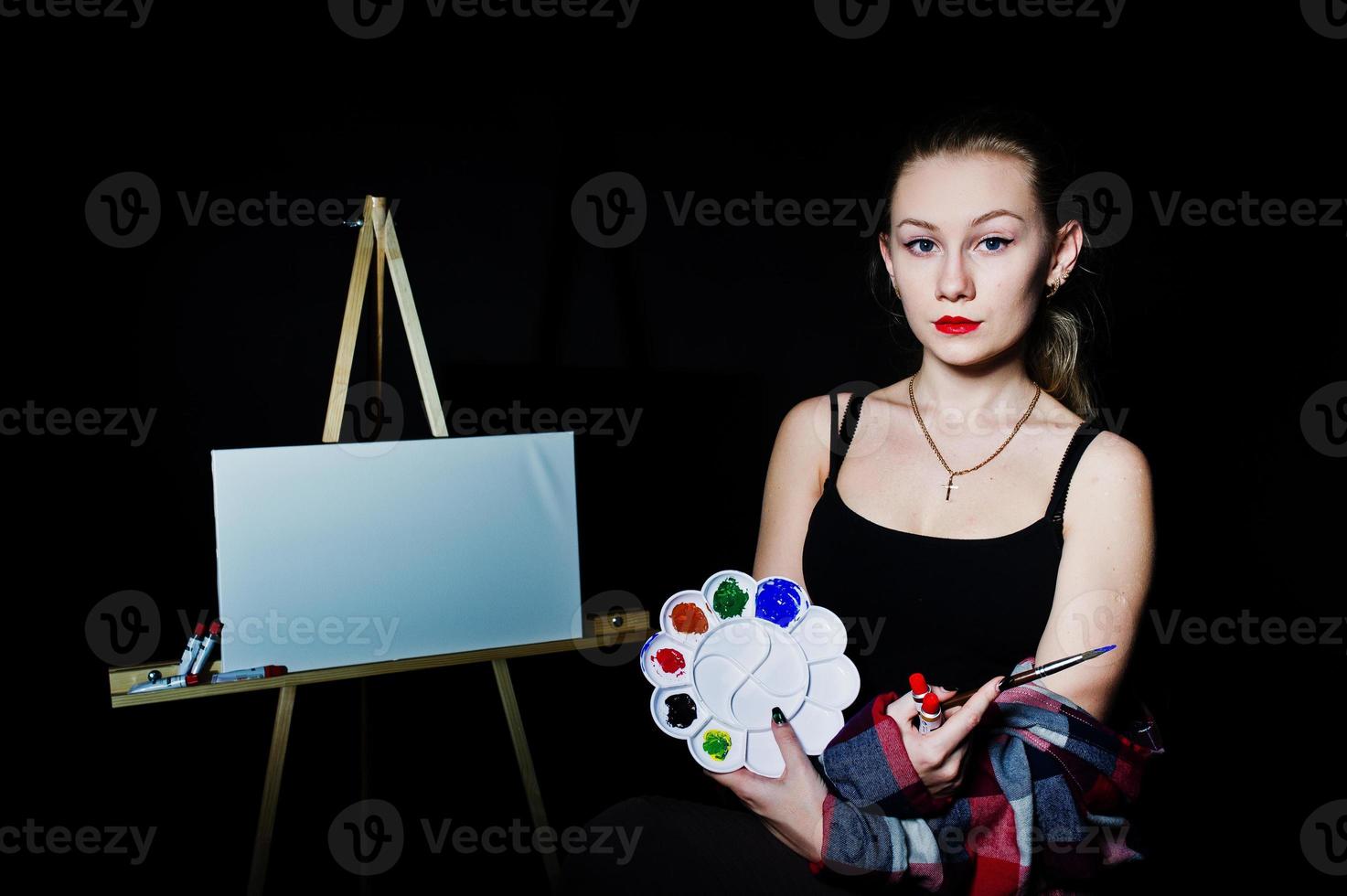 Beautiful woman artist painter with brushes and oil canvas posing in studio isolated on black. photo