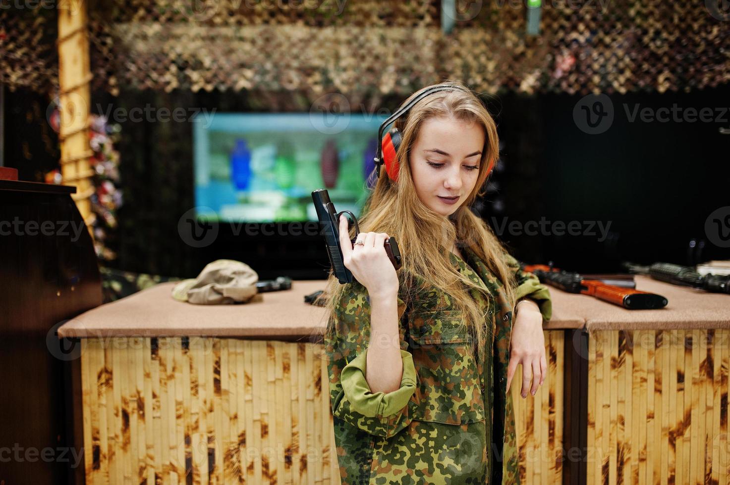 Military girl in camouflage uniform with gun at hand against army background on shooting range. photo