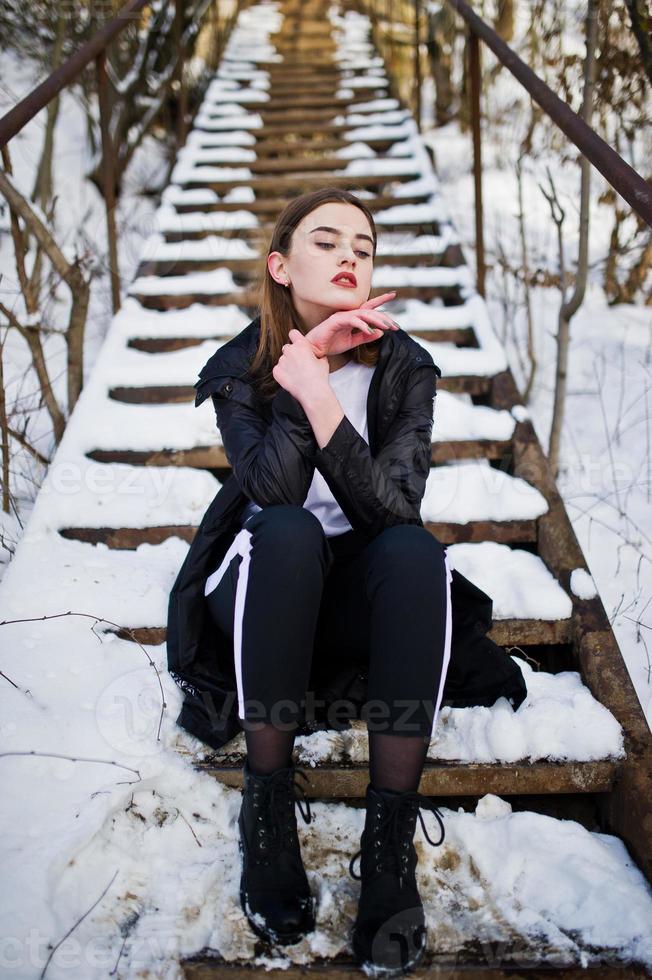modelo morena de piernas largas de moda en un largo manto negro posado al aire libre en el día de invierno. foto