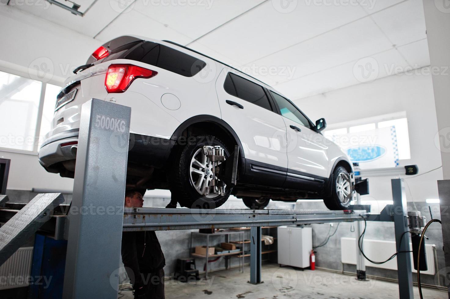 coche todoterreno americano en soporte para verificación de inclinación de alineación de ruedas en el taller de la estación de servicio. foto