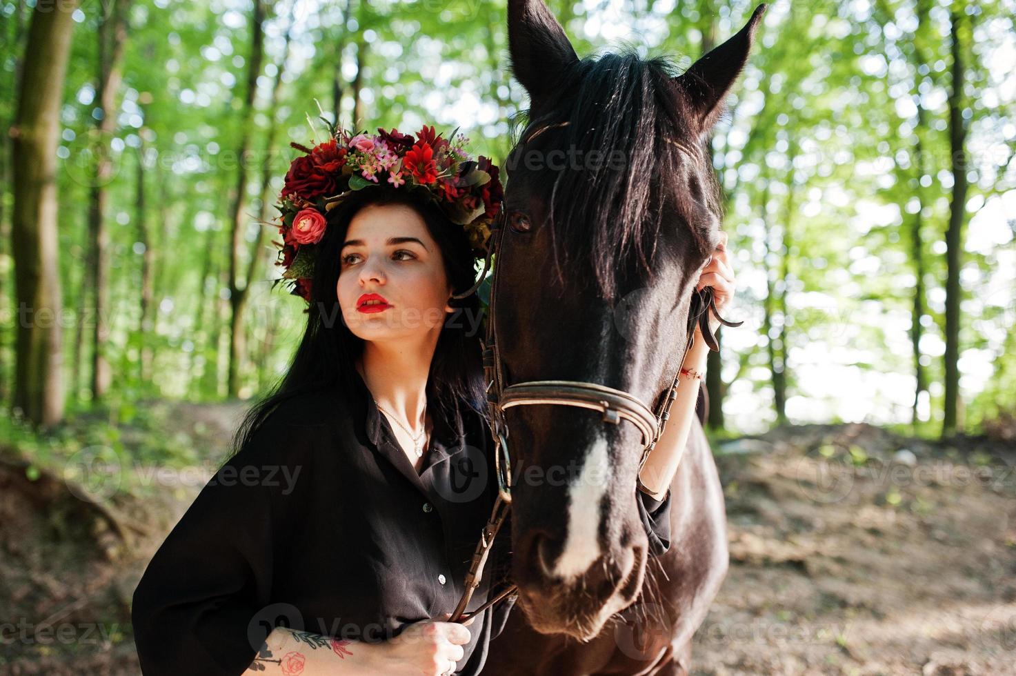 Mystical girl in wreath wear in black with horse in wood. photo