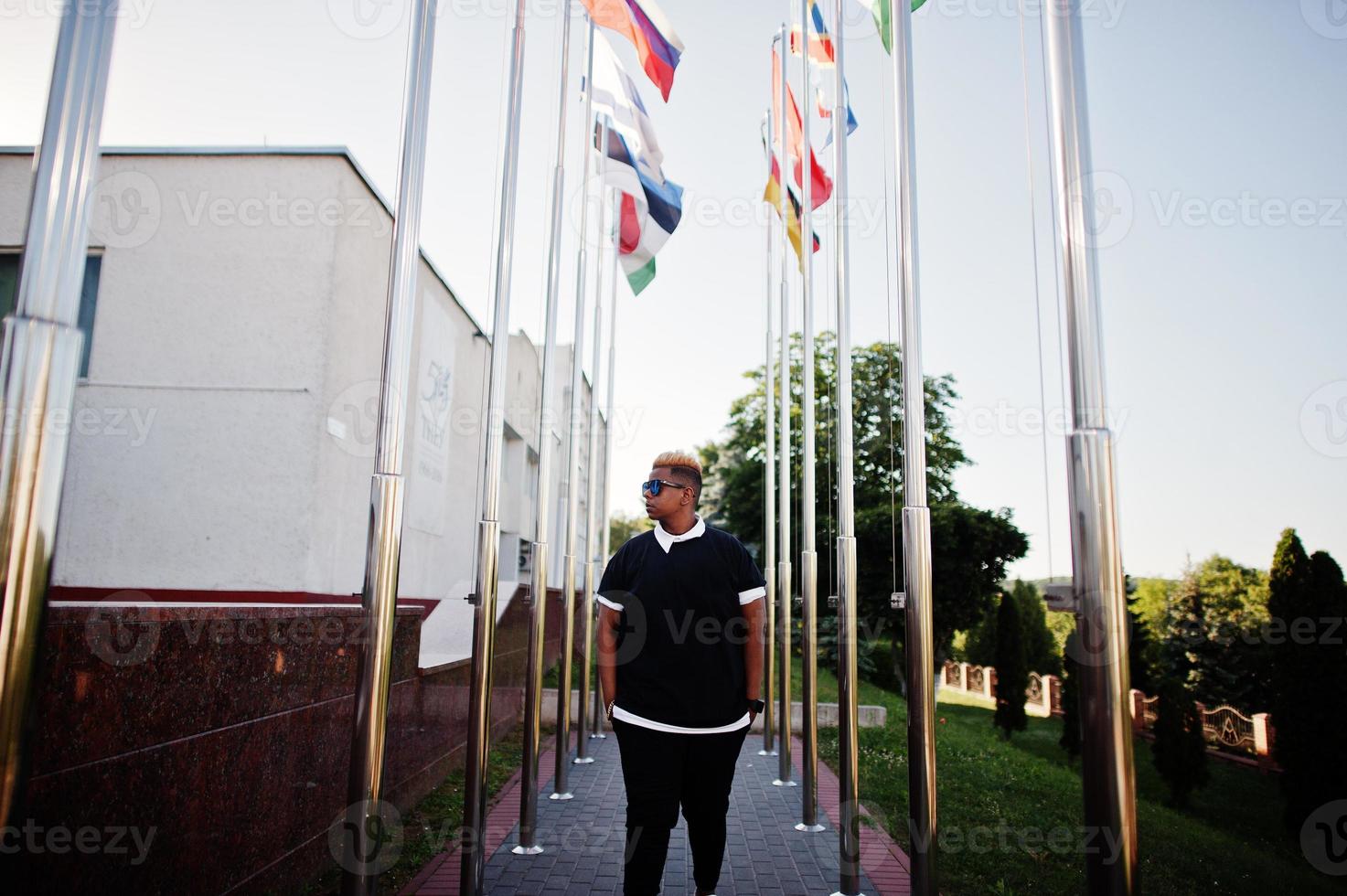 Stylish arabian muslim boy with originally hair posed on streets, against flags of different countries. photo