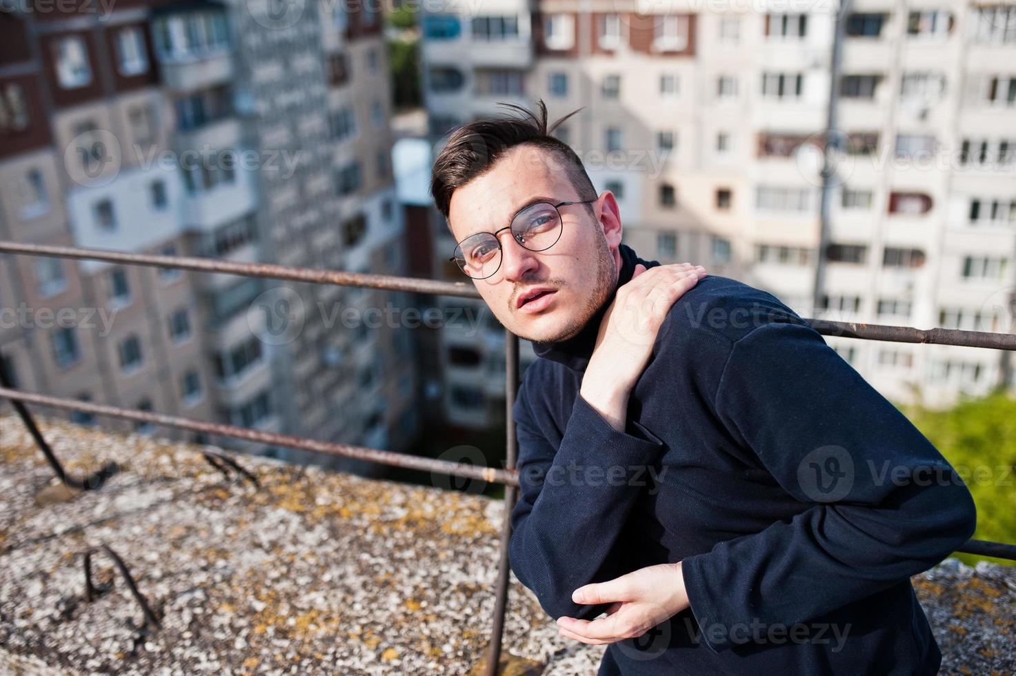 Dreamer stylish macho man in black golf and glasses posed on the roof. photo