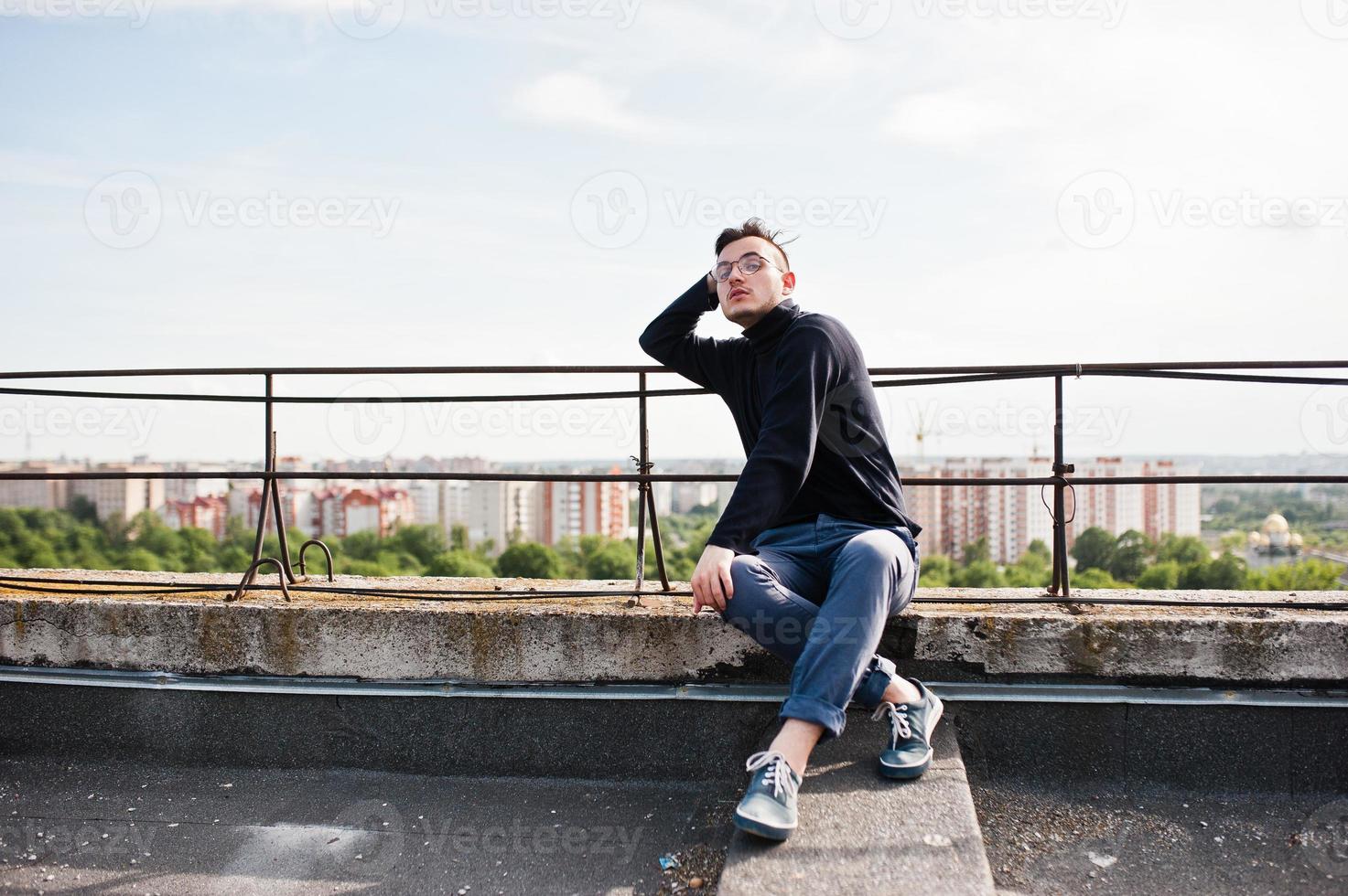 Dreamer stylish macho man in black golf and glasses posed on the roof. photo