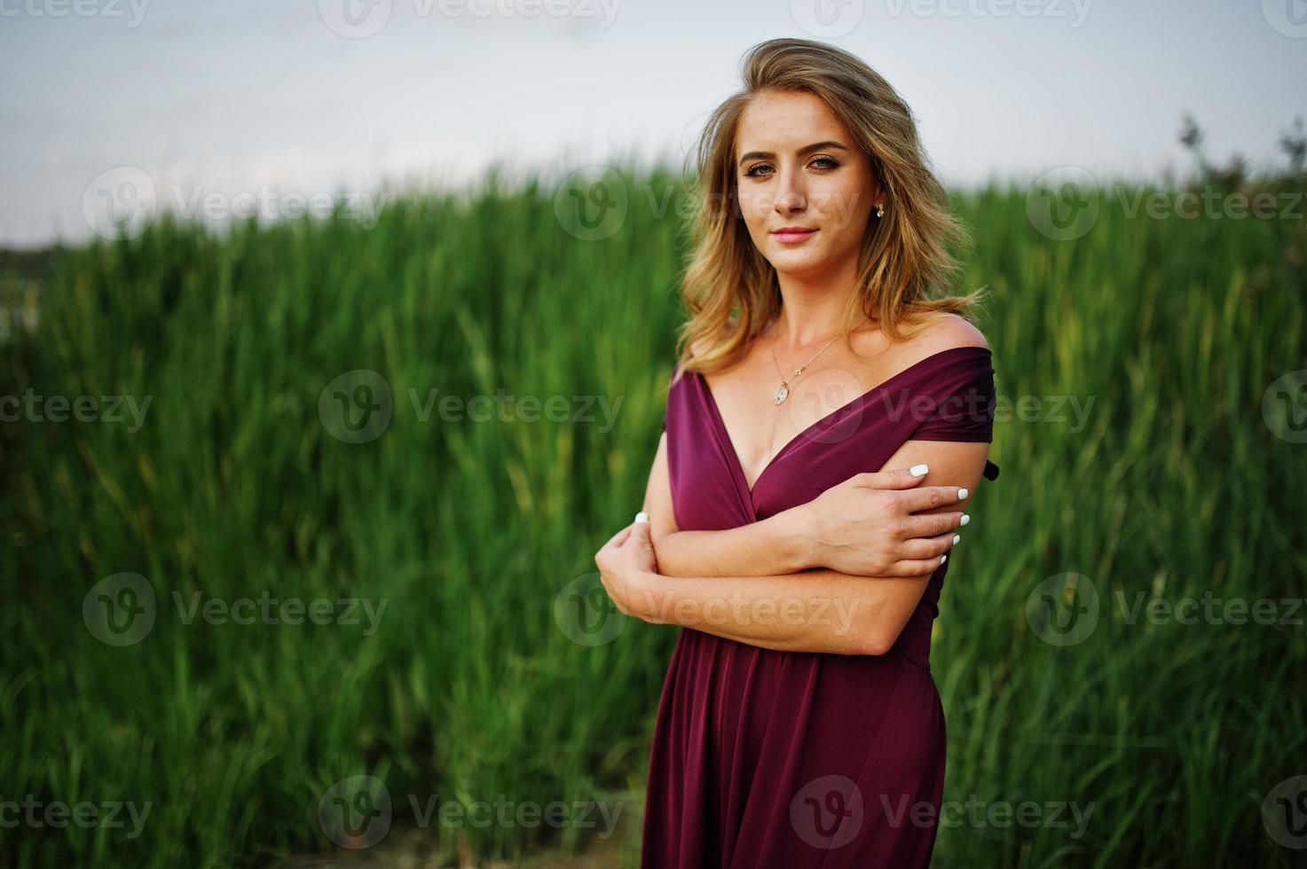 Blonde sensual woman in red marsala dress posing in the reeds. photo