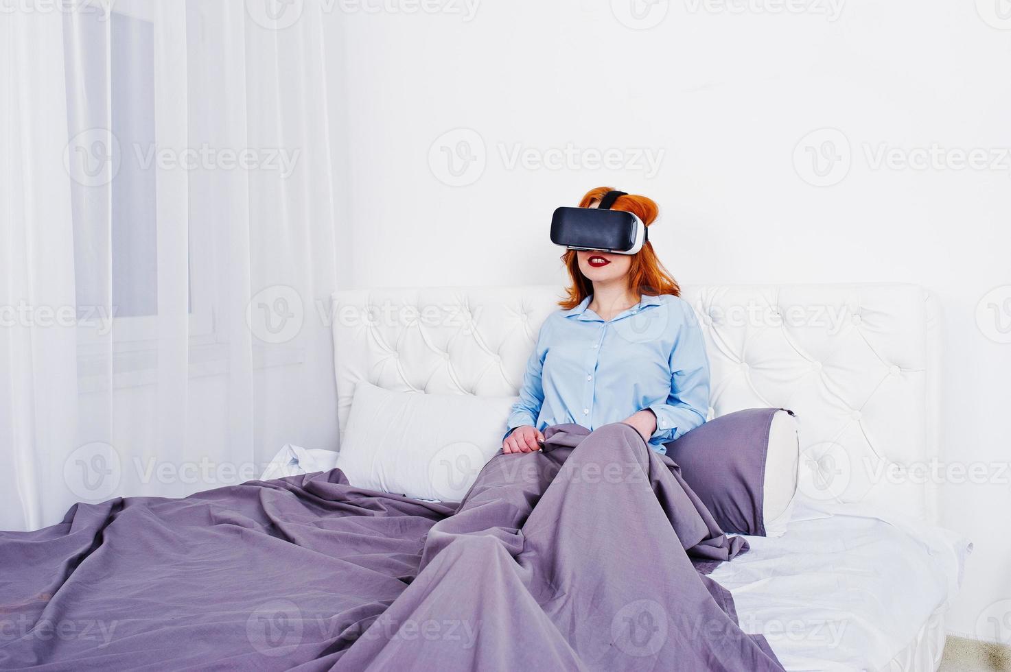 Red haired girl in bed with vr glasses at studio room. photo