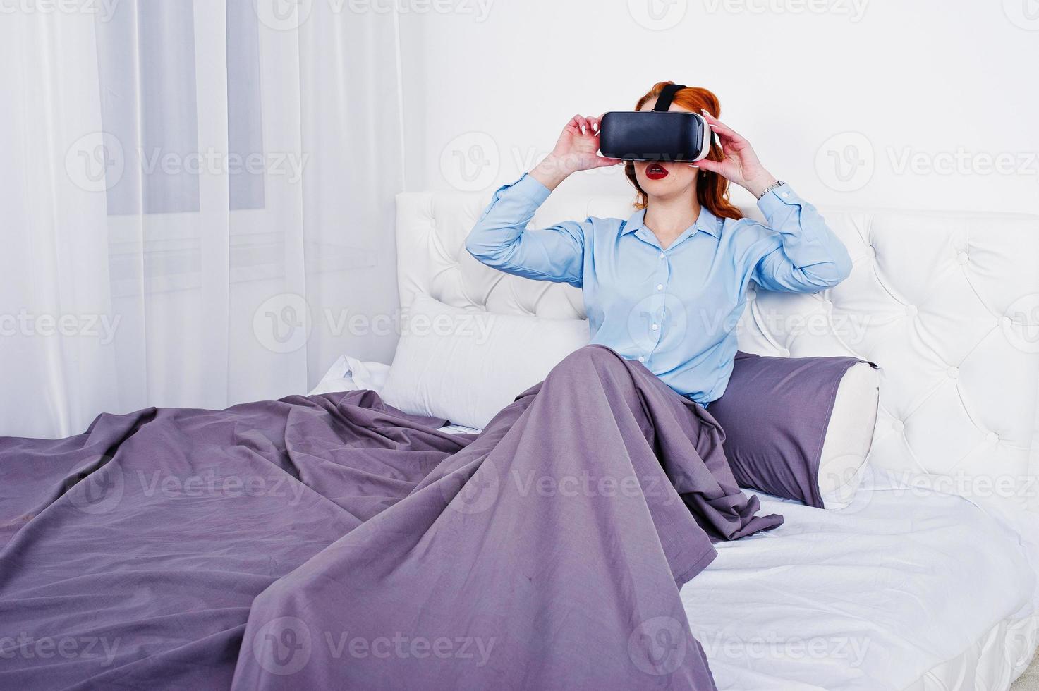 Red haired girl in bed with vr glasses at studio room. photo