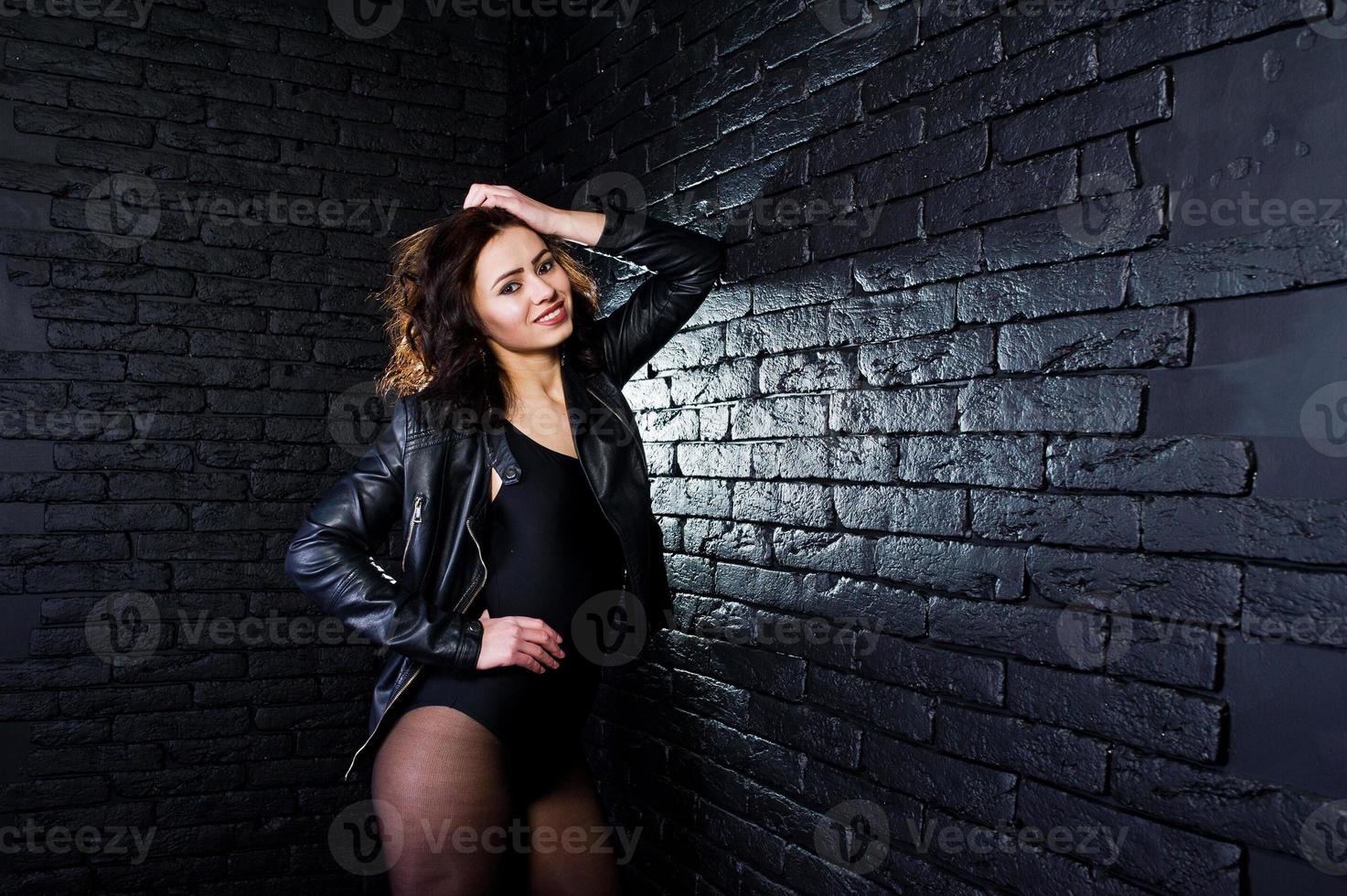 Studio portrait of sexy brunette girl in black leather jacket against brick wall. photo