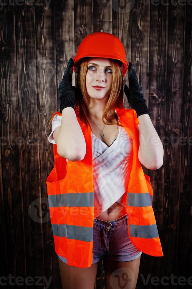 Engineer woman in orange protect helmet and building jacket against wooden background. photo