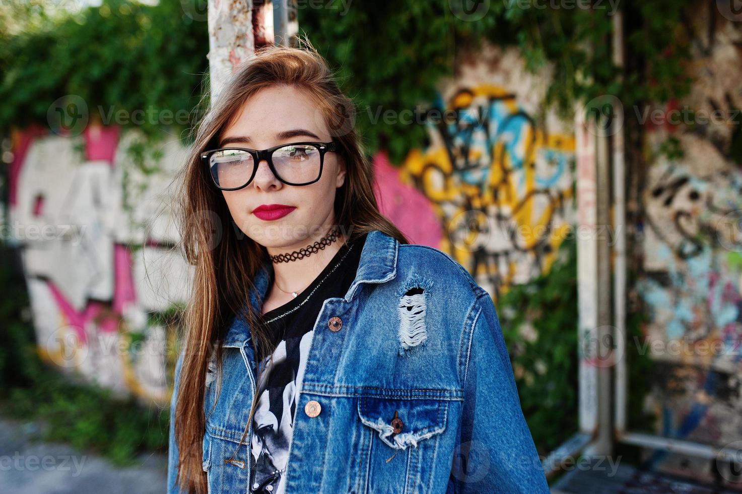 chica hipster casual con estilo en ropa de jeans y gafas contra una gran pared de graffiti. foto