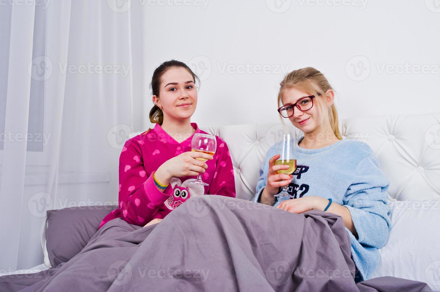 Two friends girls in pajamas having fun on bed at room. photo