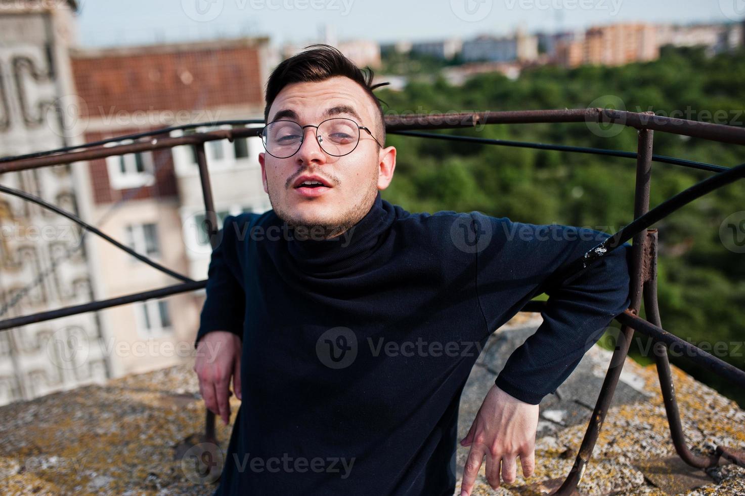 Dreamer stylish macho man in black golf and glasses posed on the roof. photo