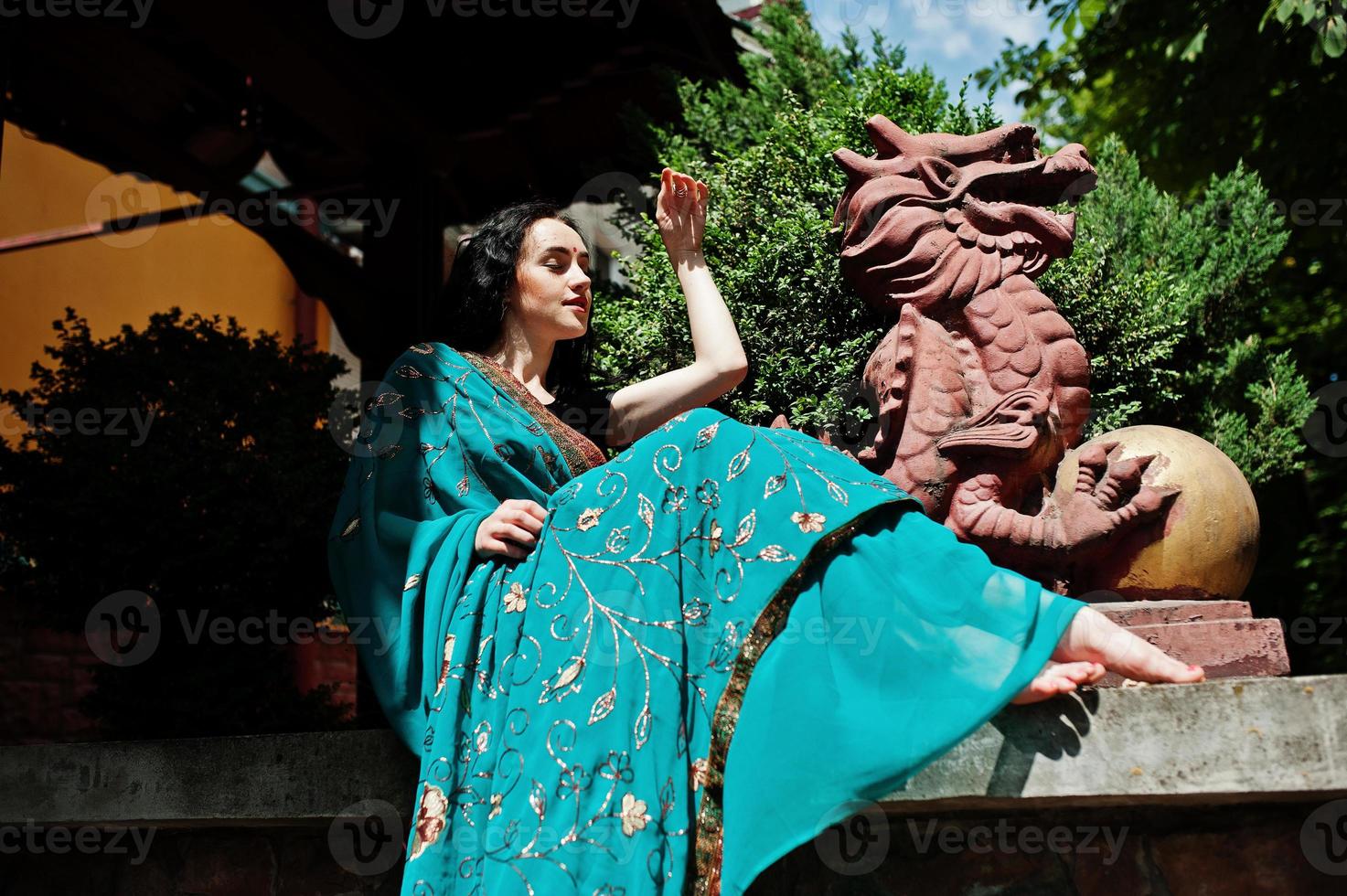 Portrait of beautiful indian brumette girl or hindu woman model against japanese traditional house and dragon figure. photo