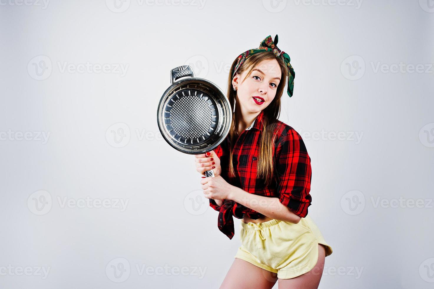 Young funny housewife in checkered shirt and yellow shorts pin up style with frying pan isolated on white background. photo