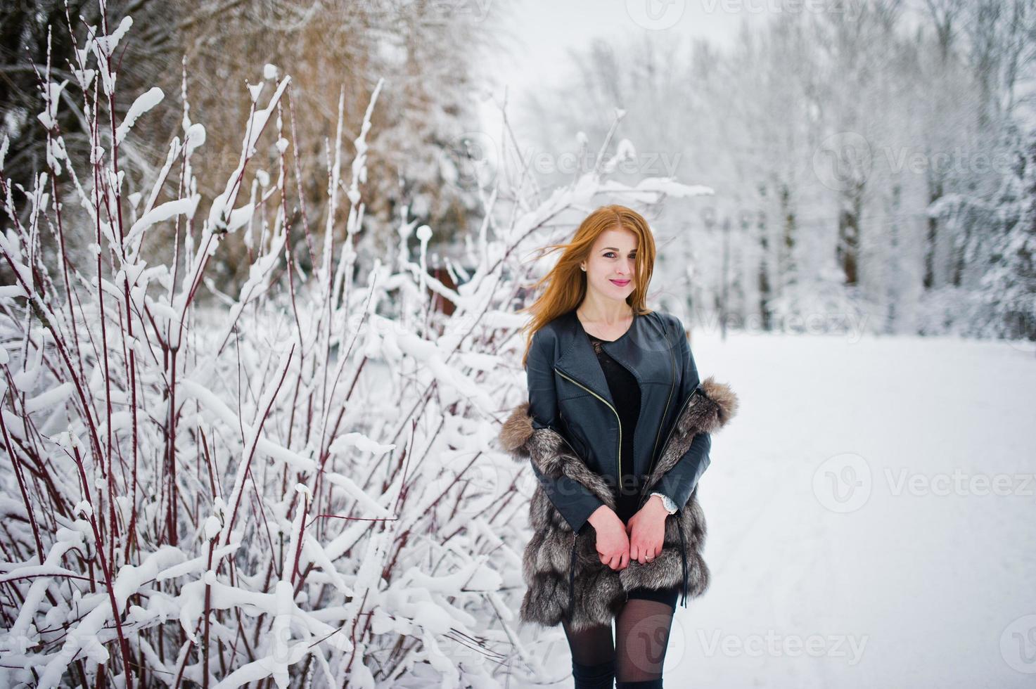 chica pelirroja con abrigo de piel caminando en el parque nevado de invierno. foto