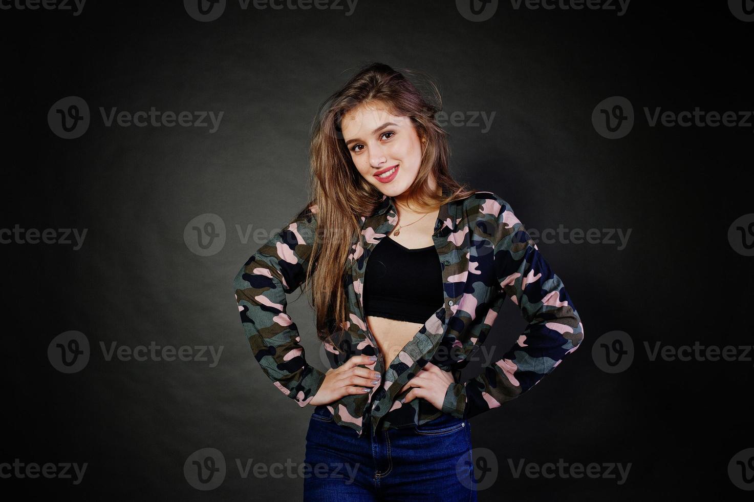 Handsome brunette girl wear military shirt and jeans, posing at studio against gray background. Studio model portrait. photo