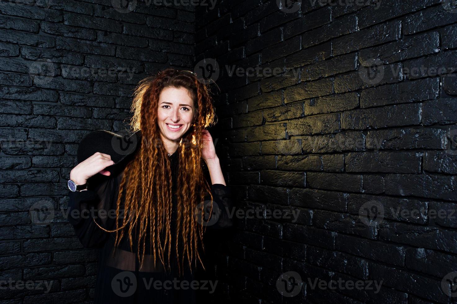 sesión de estudio de una chica de negro con rastas y sombrero sobre fondo de ladrillo. foto