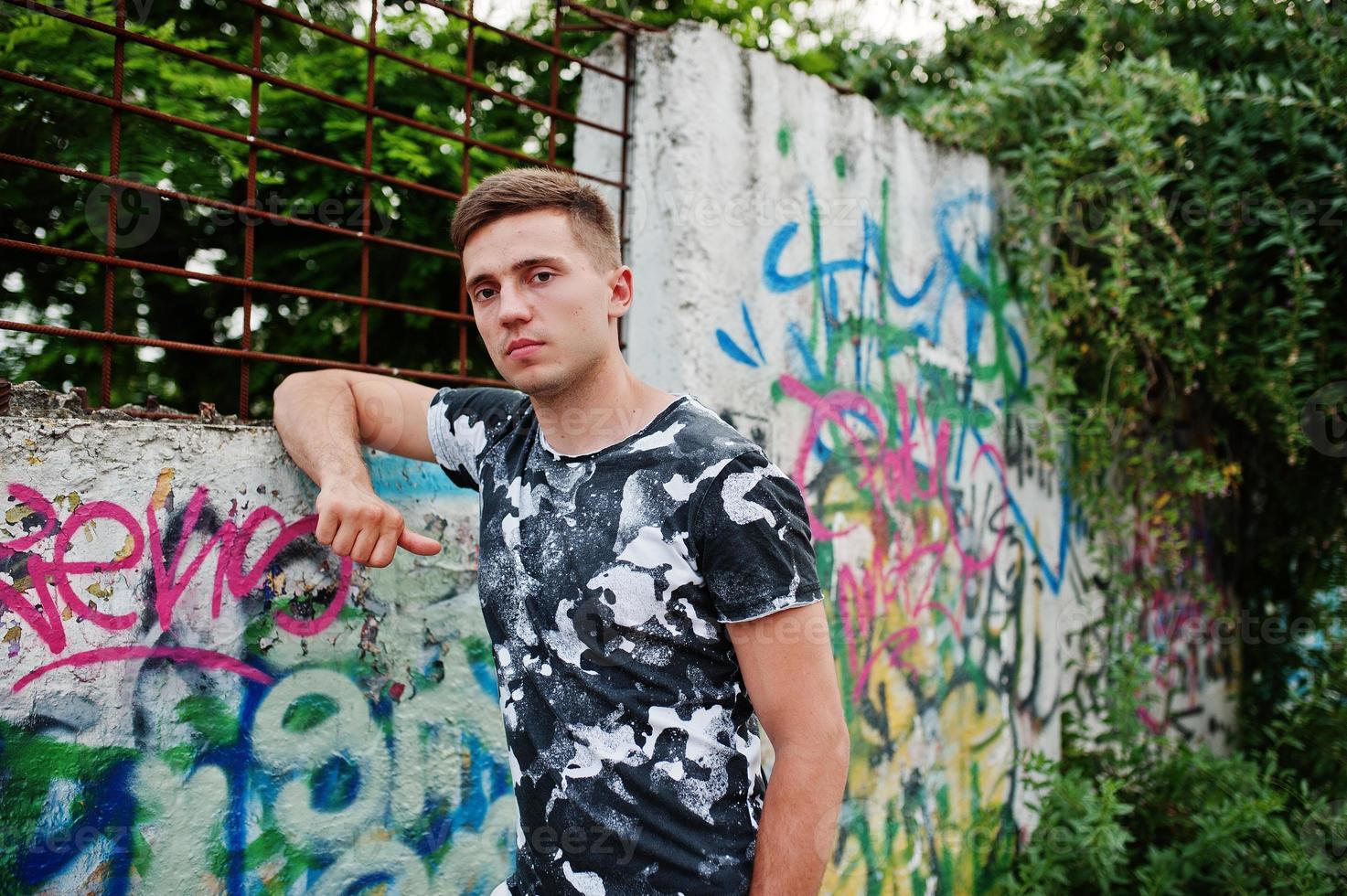 Lifestyle portrait of handsome man posing on the street of city with graffiti wall. photo