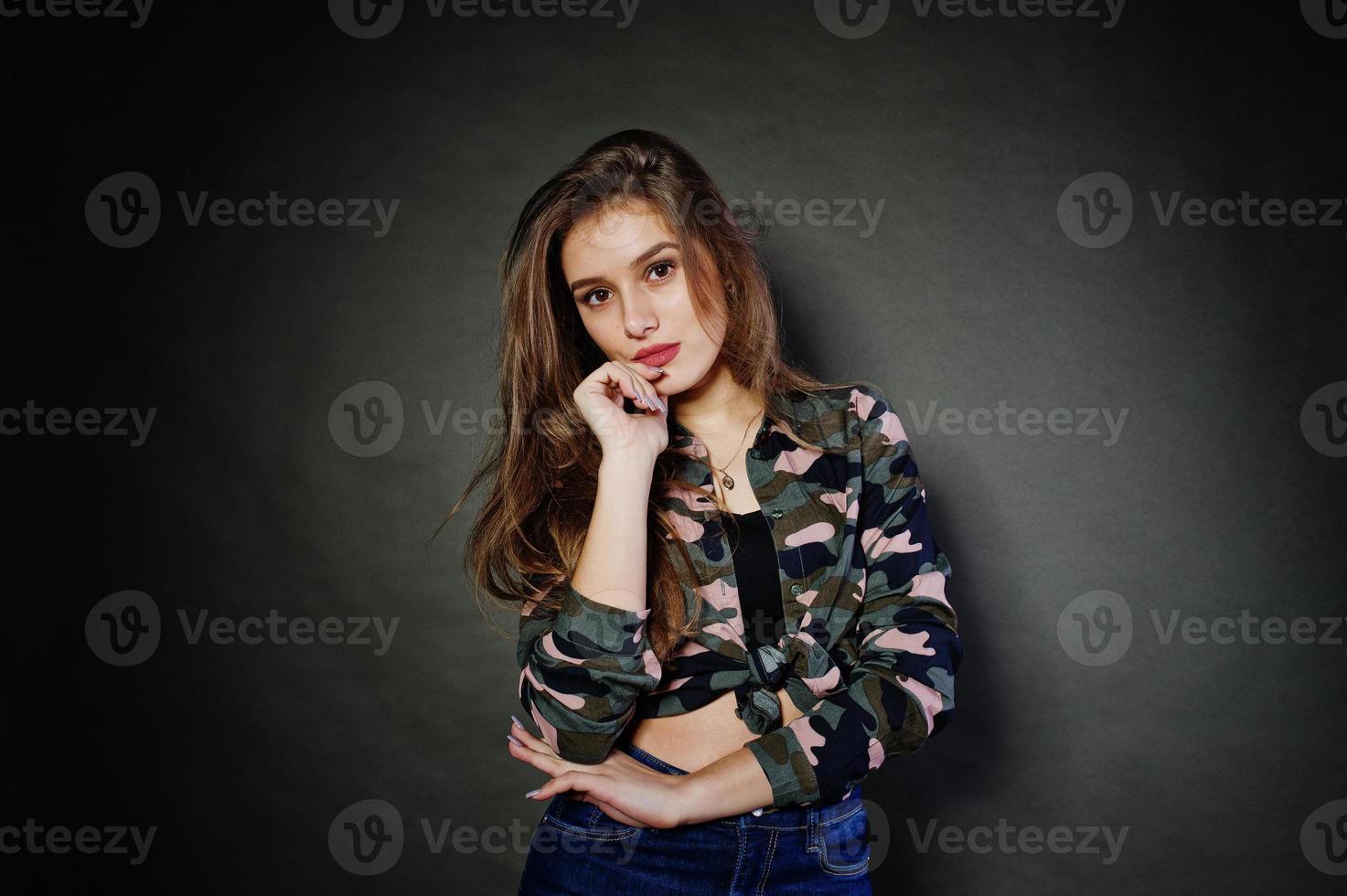 una guapa morena usa camisa militar y jeans, posando en el estudio con fondo gris. retrato de modelo de estudio. foto