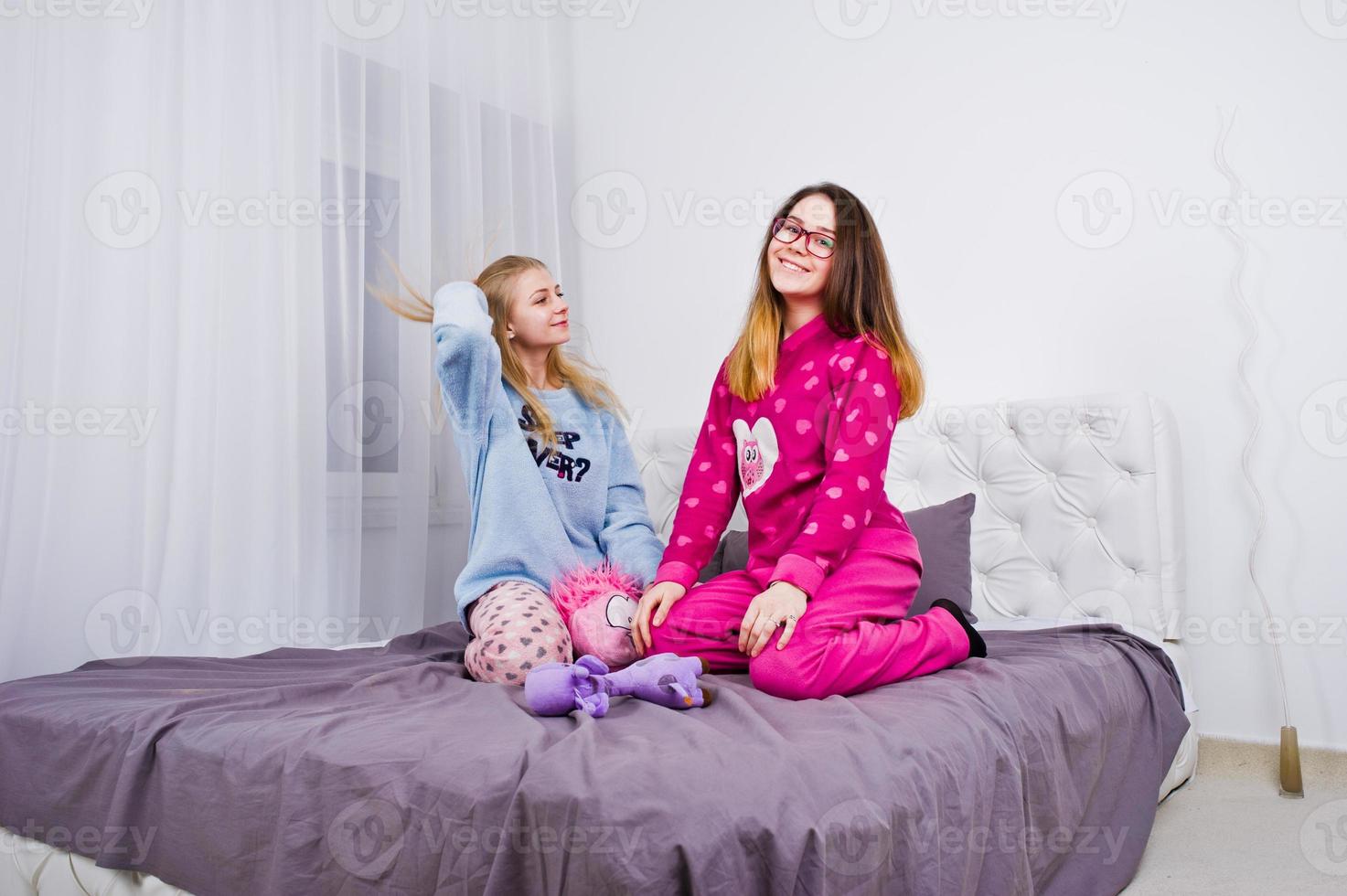 Two friends girls in pajamas having fun on bed at room. photo