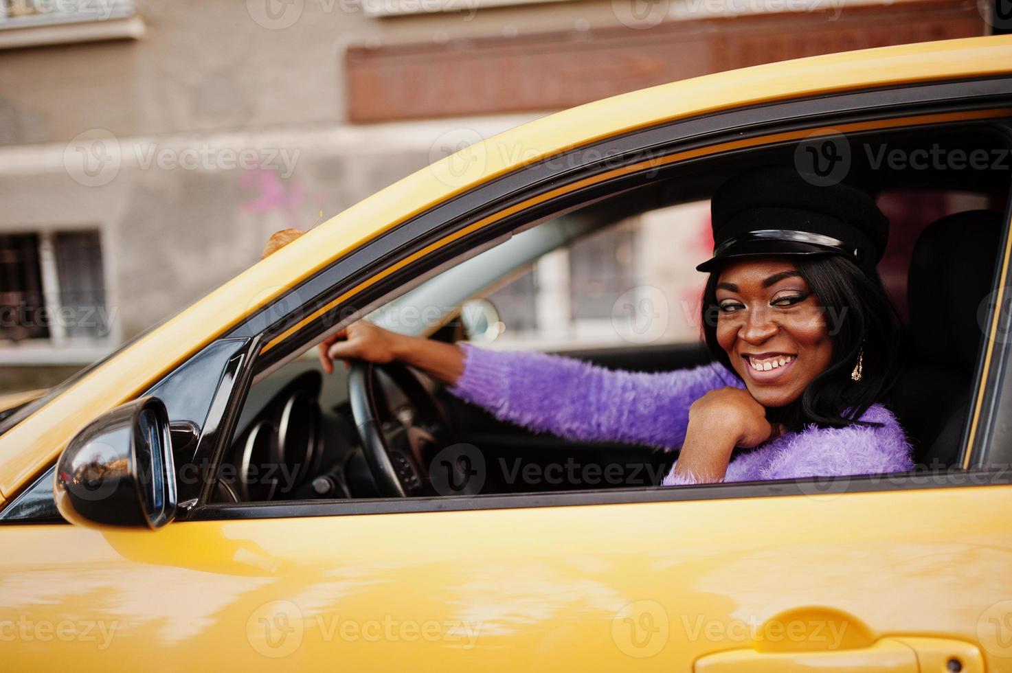 African american woman at violet dress and cap posed at yellow car. photo