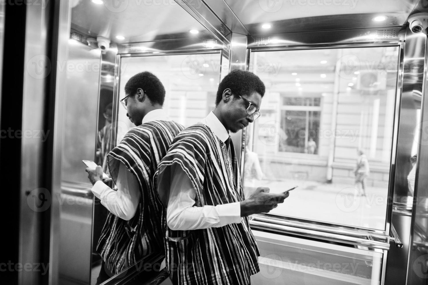 African man in traditional clothes and glasses with mobile phone at elavator or modern lift. photo