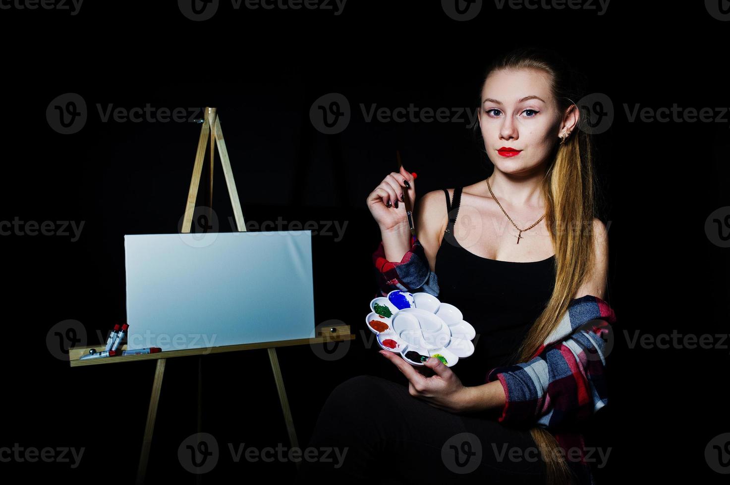 Beautiful woman artist painter with brushes and oil canvas posing in studio isolated on black. photo
