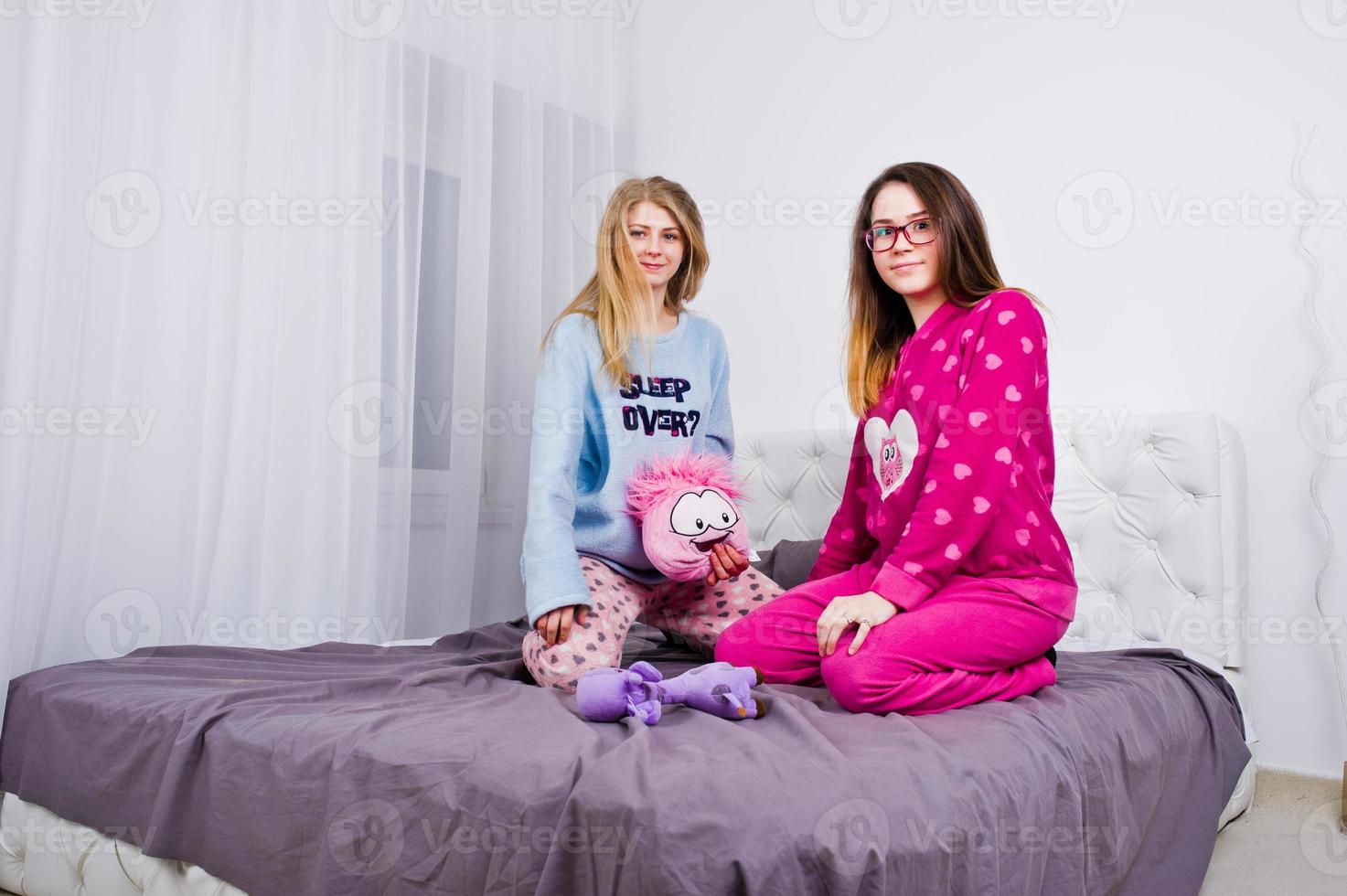 Two friends girls in pajamas having fun on bed at room. photo