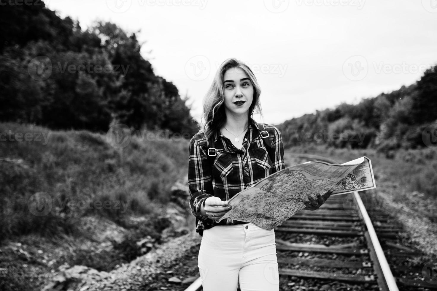 retrato de una linda chica rubia con camisa de tartán caminando por el ferrocarril con un mapa en las manos. foto