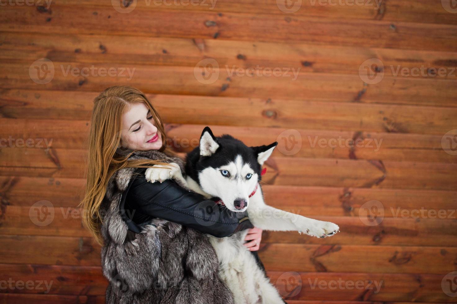 Red haired girl with husky dog against wooden wall. photo