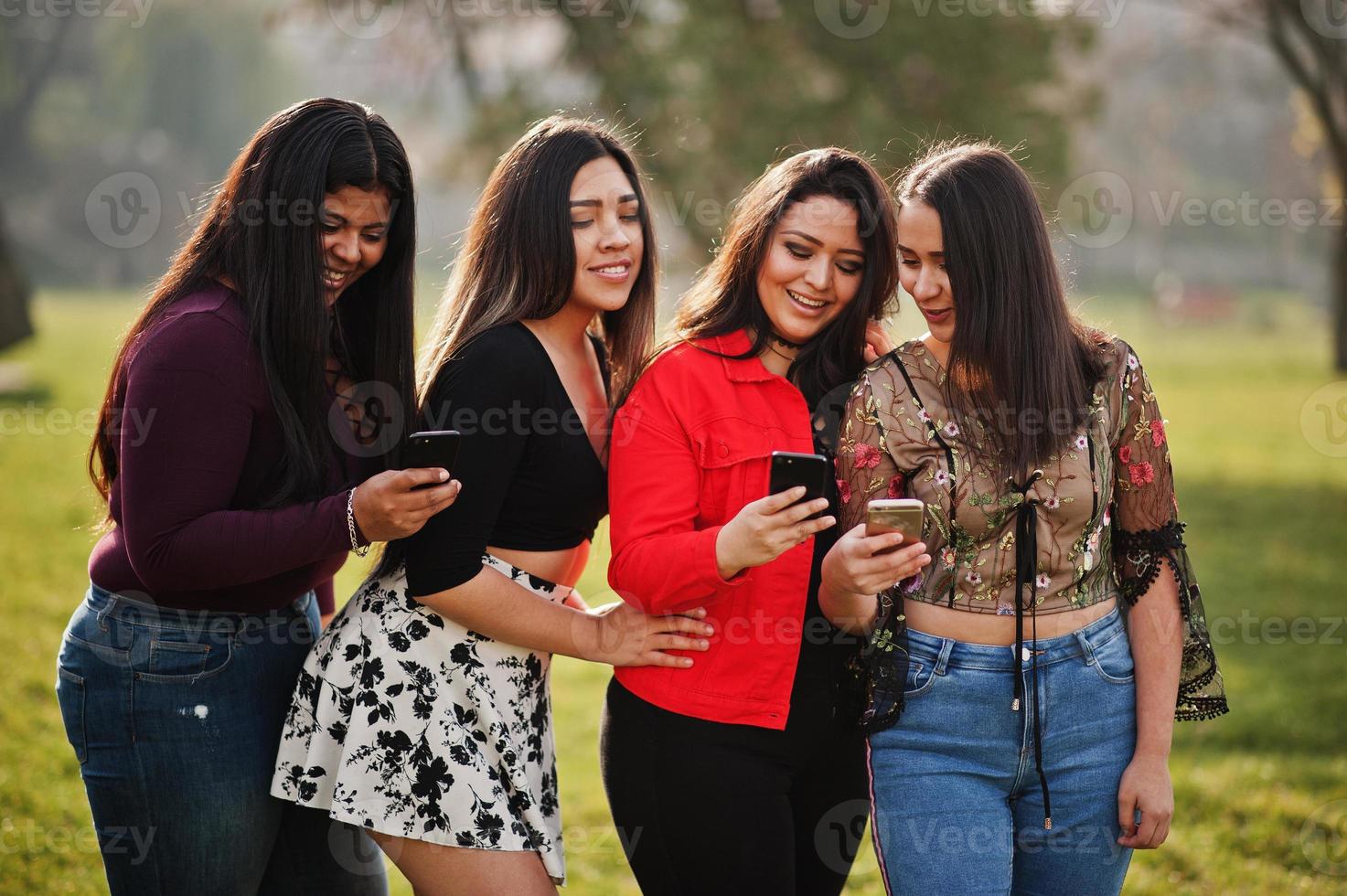 grupo de cuatro chicas latinas felices y bonitas de ecuador posaron en la calle y mirando teléfonos móviles. foto