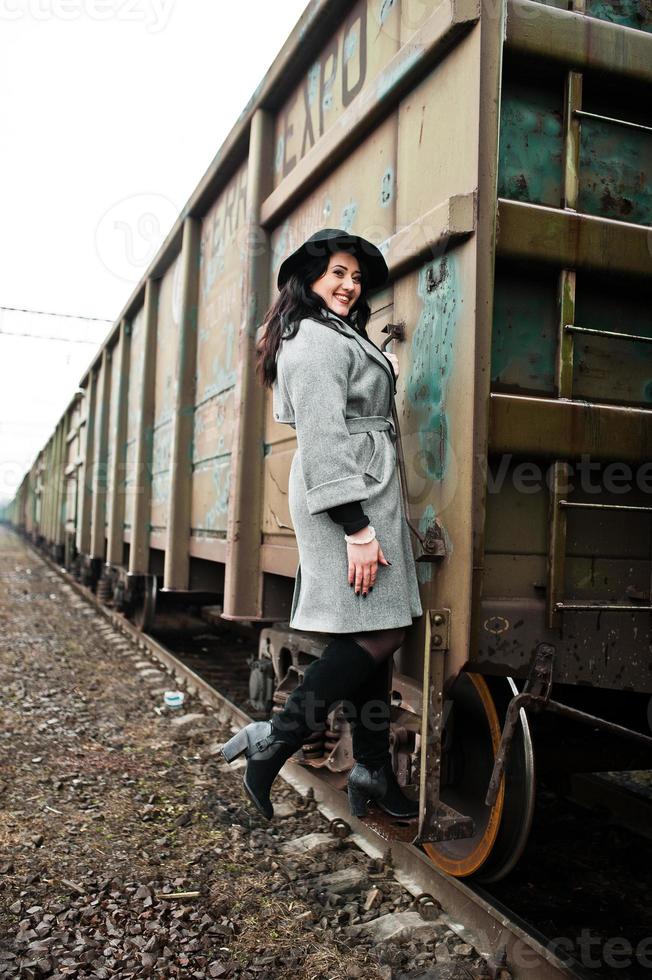 chica morena con abrigo gris con sombrero en la estación de tren. foto