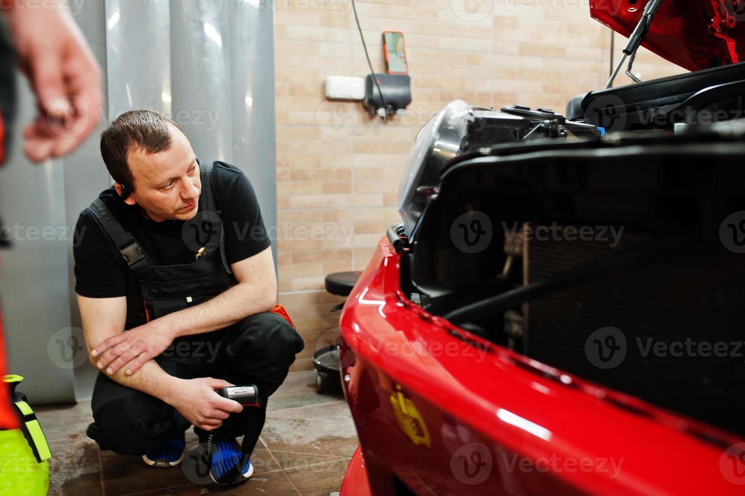 Car service worker put anti gravel film on a red car body at the detailing vehicle workshop. Car protection with special films. photo