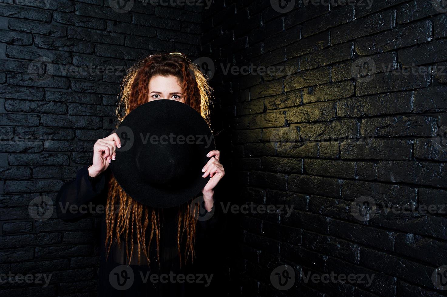 Studio shoot of girl in black with dreads and hat on brick background. photo