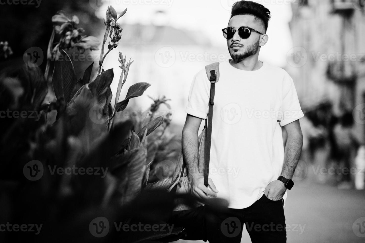 elegante hombre de barba india con camiseta rosa, gafas de sol y mochila. modelo india posó al aire libre en las calles de la ciudad del atardecer. foto