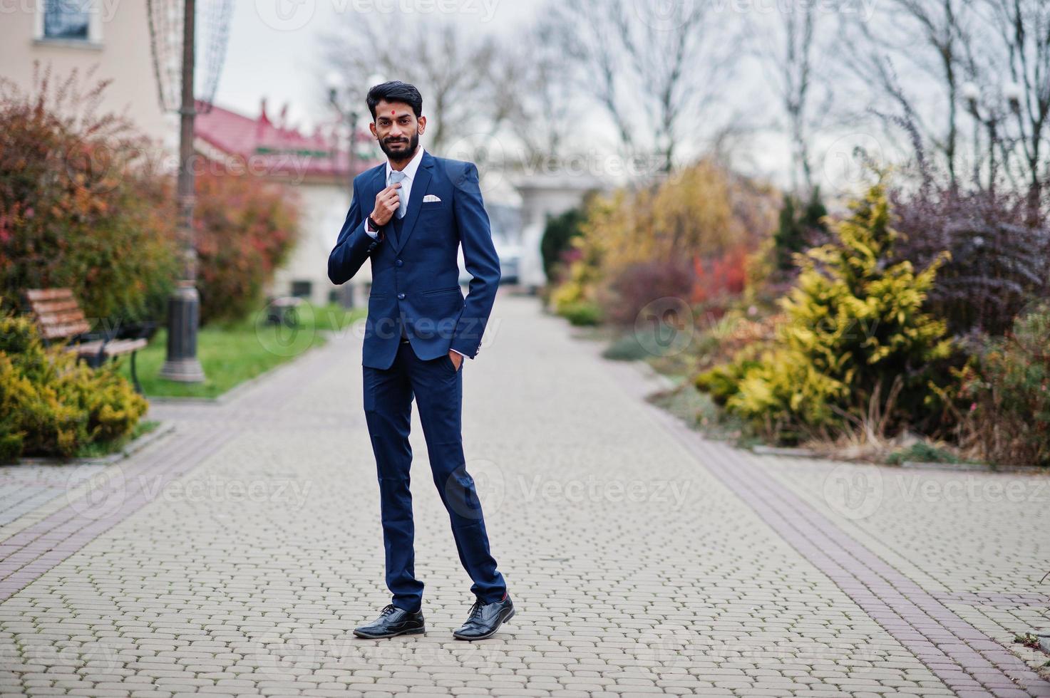 Stylish beard indian man with bindi on forehead, wear on blue suit posed outdoor. photo