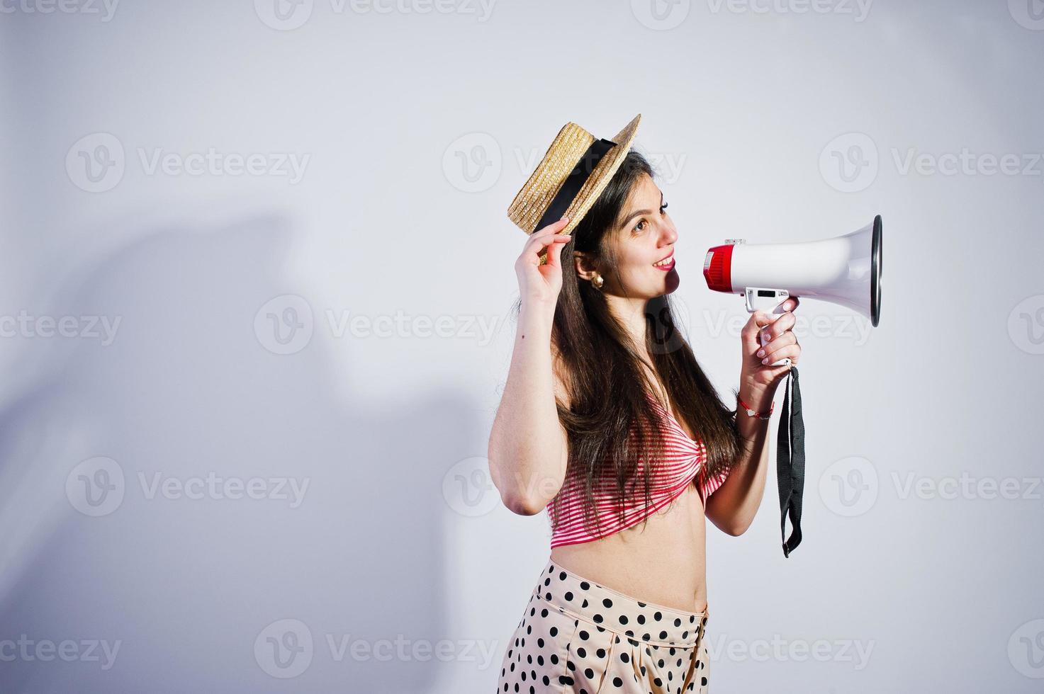 Portrait of a gorgeous young girl in swimming suit and hat talks into megaphone in studio. photo