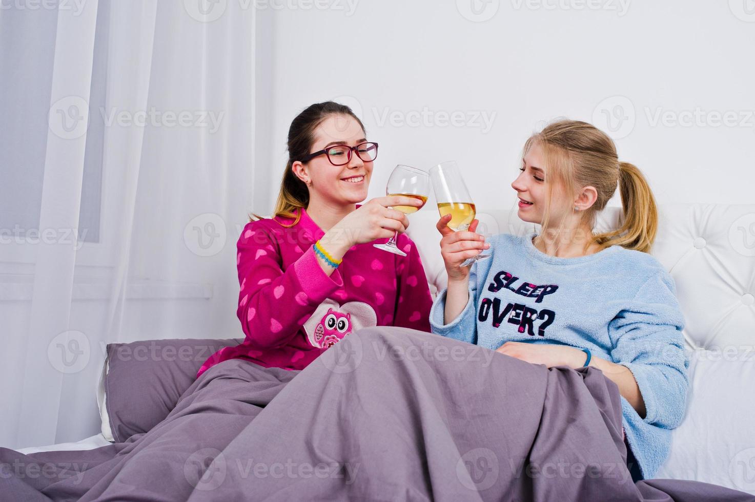 Two friends girls in pajamas having fun on bed at room. photo