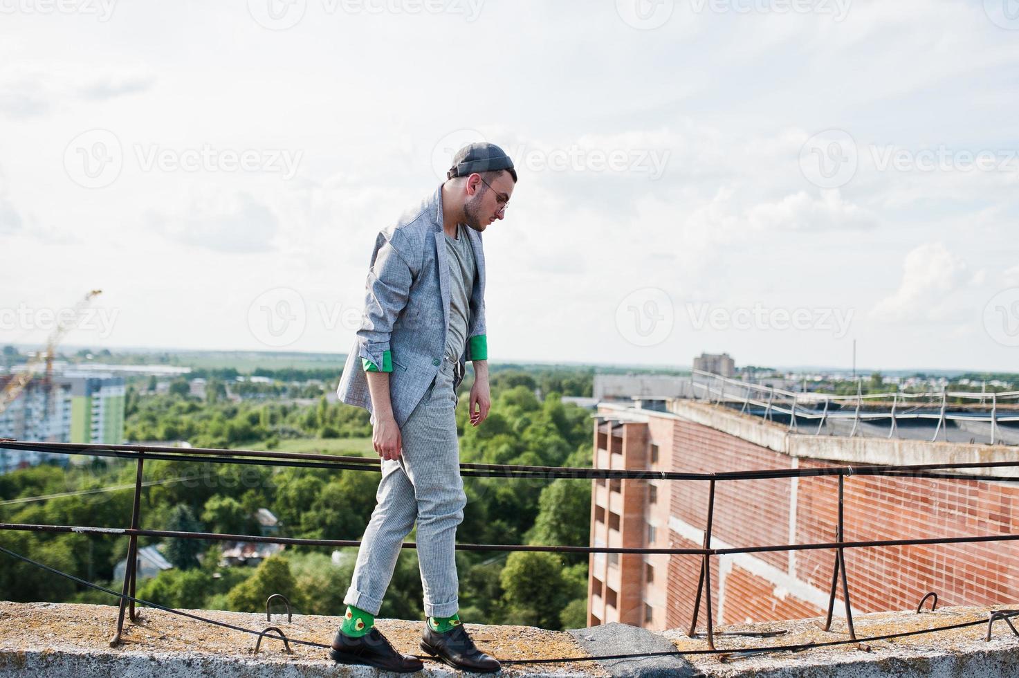 Dreamer stylish macho man in gray suit, hat and glasses posed on the roof. photo