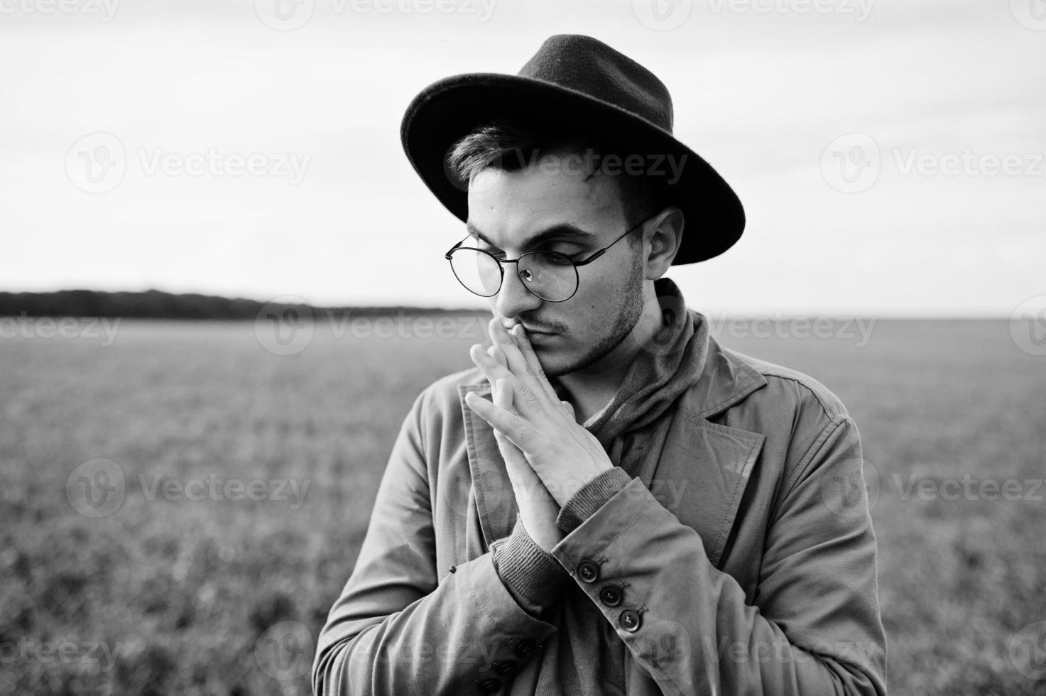 Stylish man in glasses, brown jacket and hat posed on green field