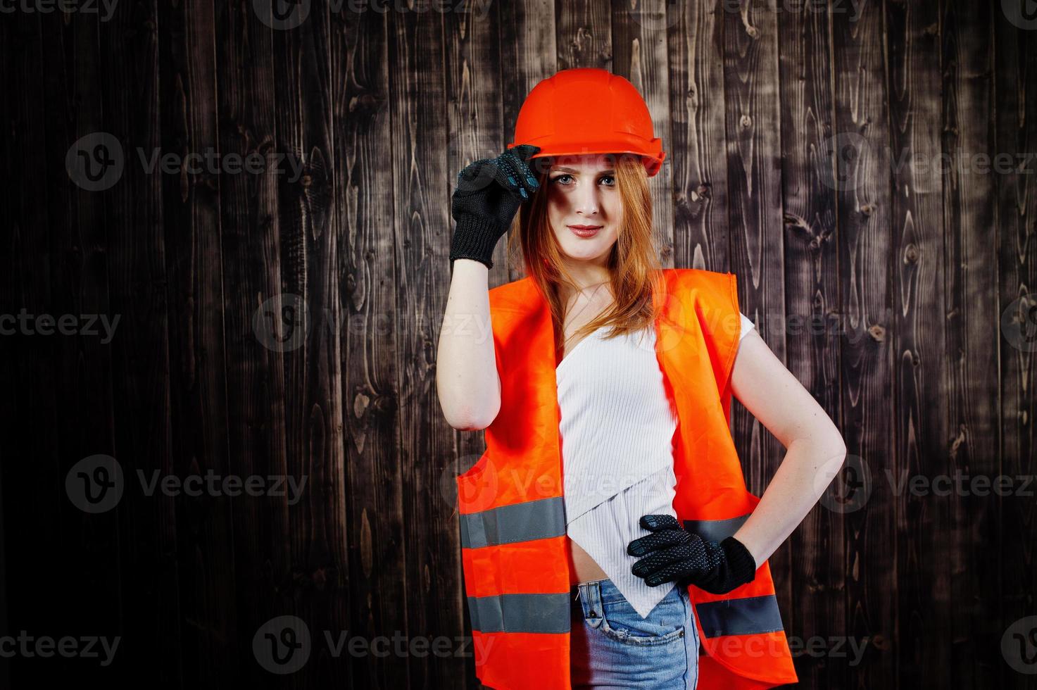 Engineer woman in orange protect helmet and building jacket against wooden background. photo