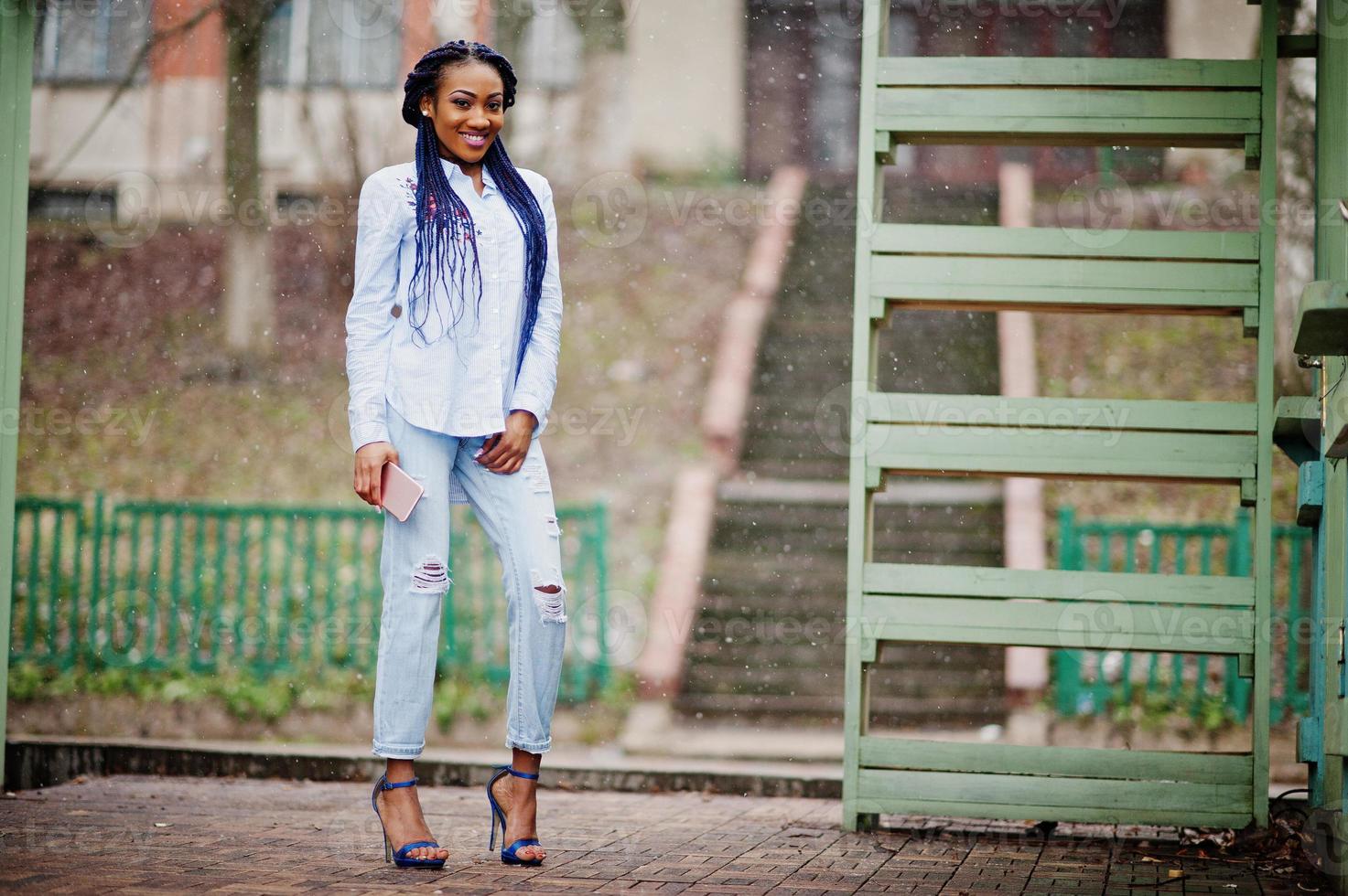 Stylish african american girl with dreads holding mobile phone at hand, outdoor snowy weather. photo