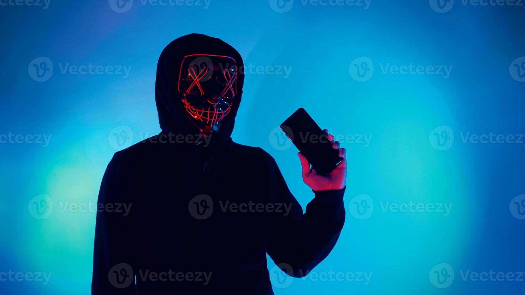 Anonymous hacker and face mask with smartphone in hand. photo