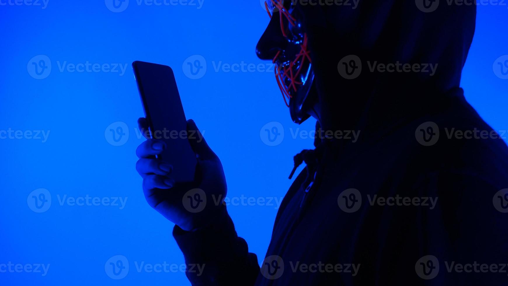 Anonymous hacker and face mask with smartphone in hand. photo