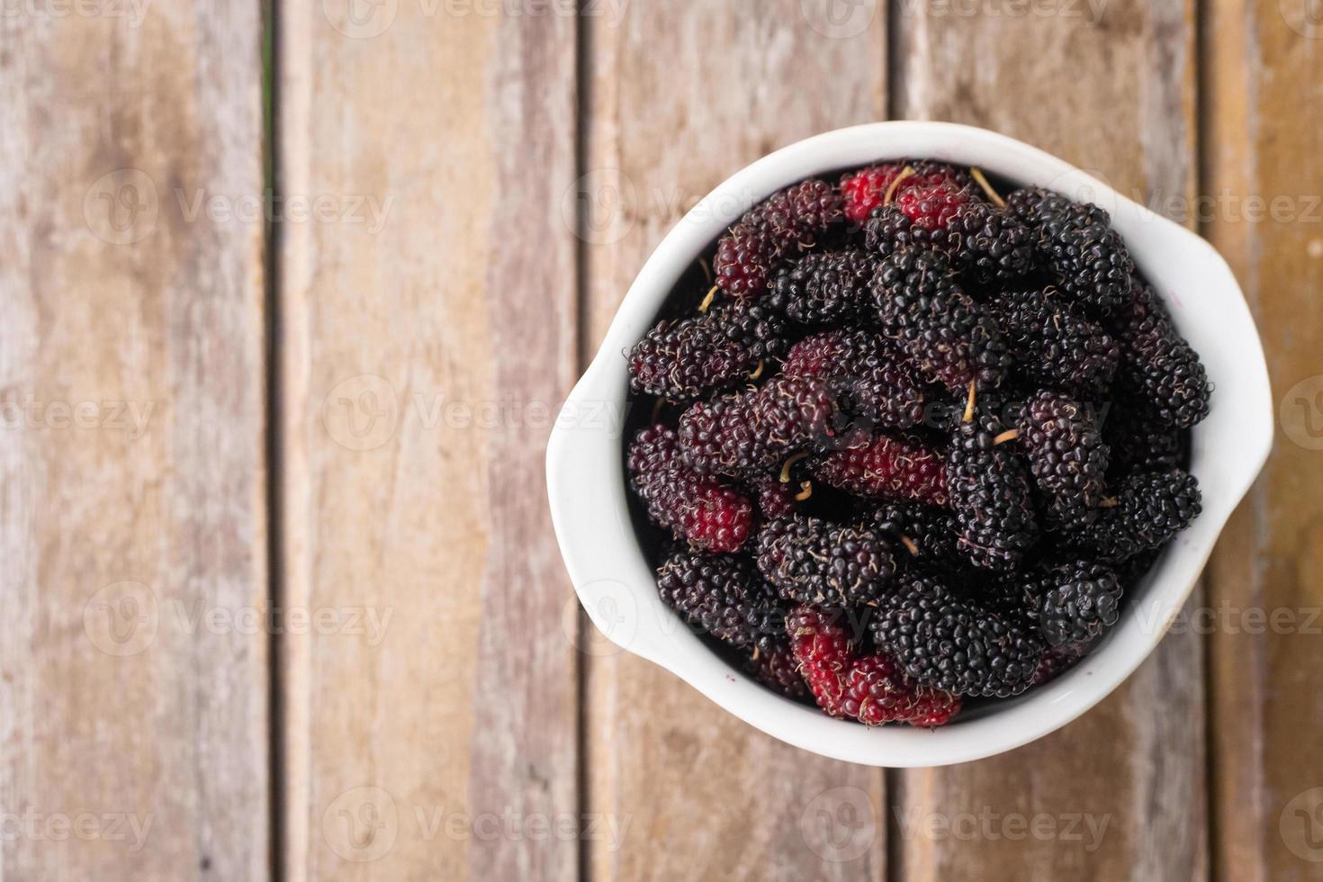 The mulberry fruit in white bowl on wood table. photo