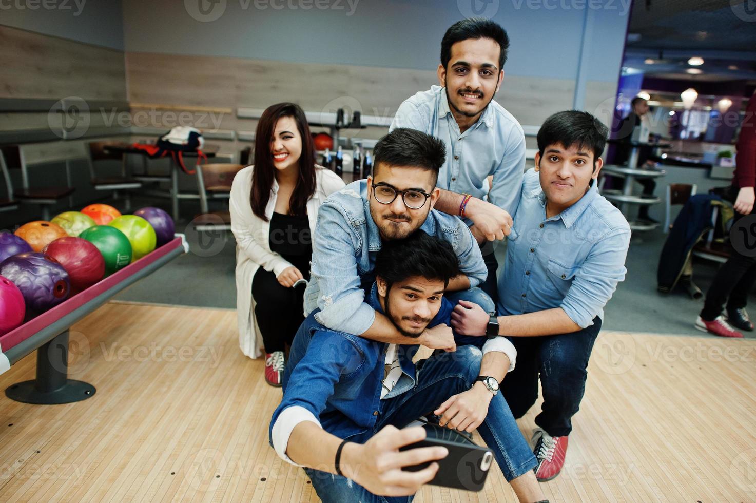 Group of five south asian peoples having rest and fun at bowling club. Making selfie by phone. photo