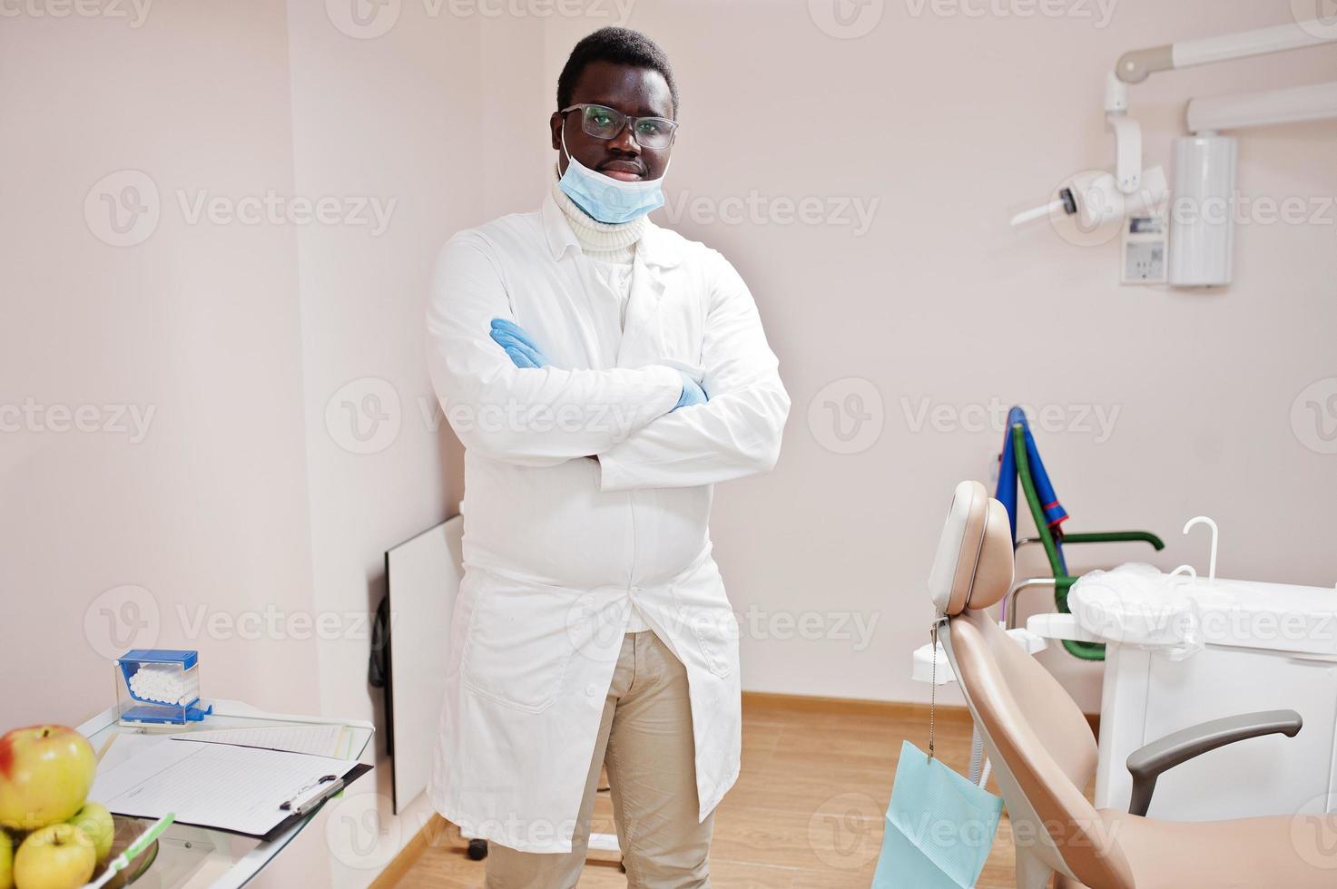 African american male doctor in glasses and mask posed in clinic with crossed arms. photo