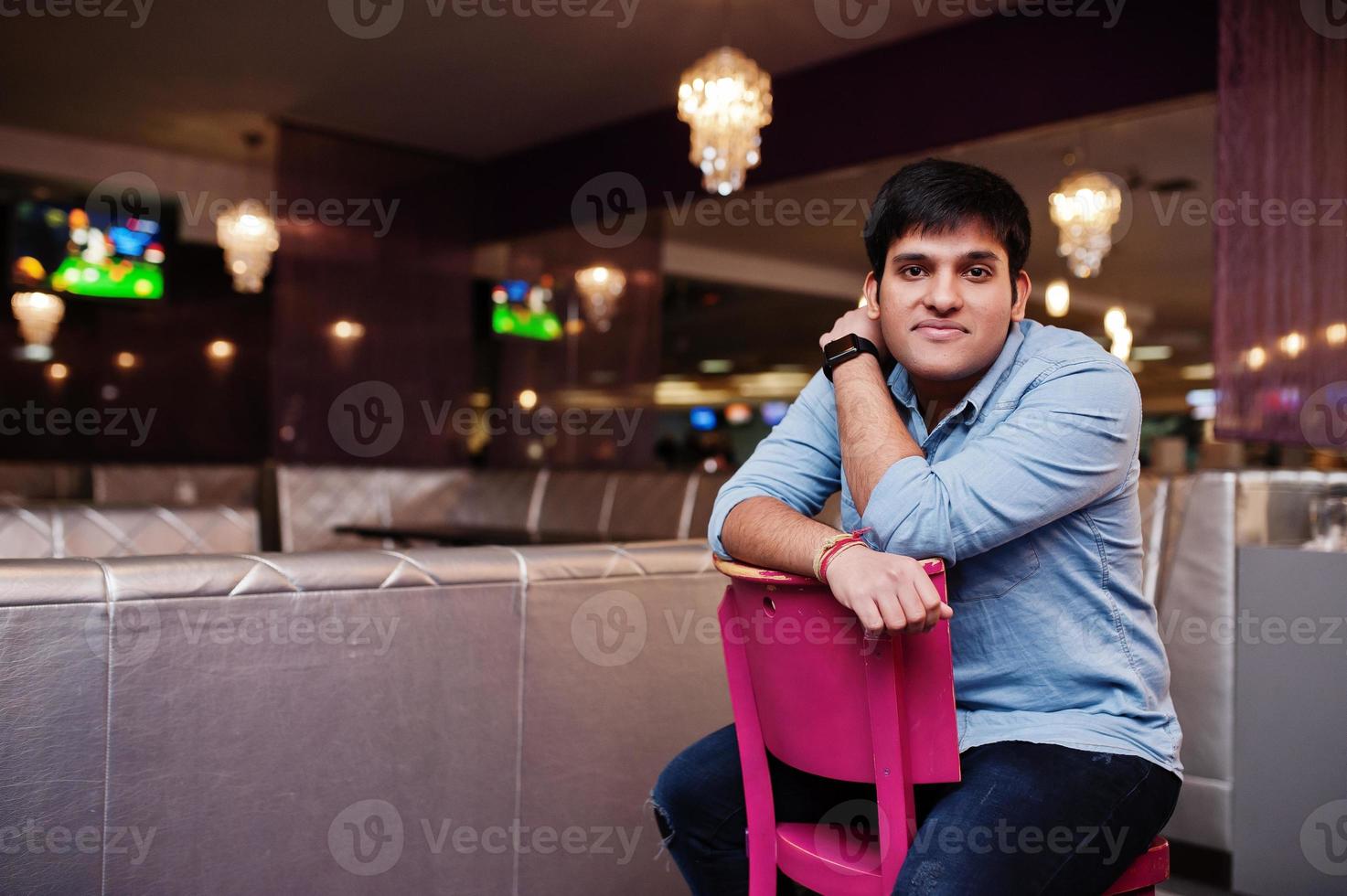 elegante hombre asiático vestido con camisa de jeans sentado en una silla contra el bar en el club. foto