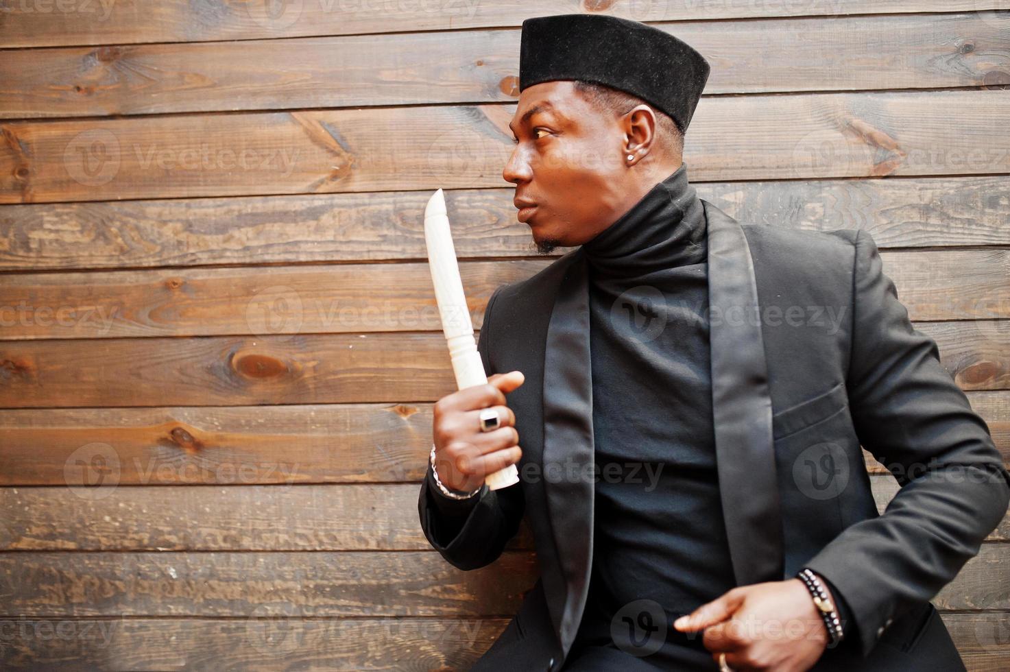 Strong powerful african american man in black suit and turtleneck and cap, with elephant tusk. photo